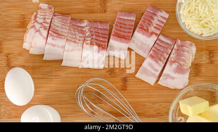 Rohe becon-Scheiben, Eier, Butter und Käse. Kochen des Frühstücks, Zutaten aus der Nähe auf einem Holzbrett, flach liegend Stockfoto