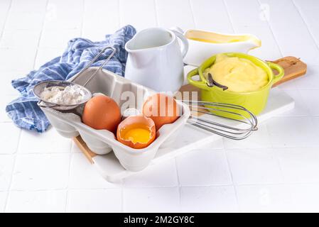 Hausgemachte Creme mit Zutaten - Vanille, Milch und Eier. Süße Creme anglaise Dessertkoch Hintergrund, auf weißem Küchentisch Kopierbereich Stockfoto