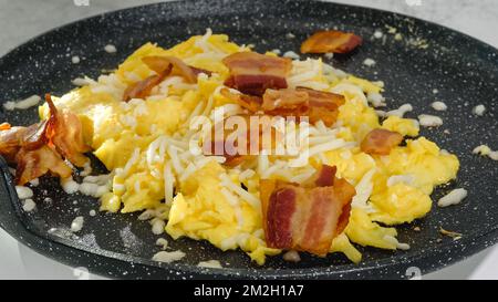 Rührei, gebraten mit Käse und Speck, Nahaufnahme auf einer Pfanne. Stockfoto