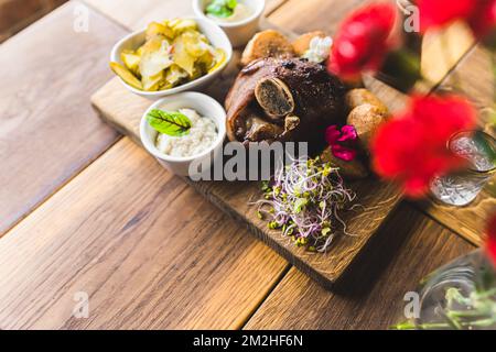 Im Ofen gebackene Schweineknöchel, serviert auf einem Holzbrett zusammen mit Quelle, Kartoffeln und Gemüse. Polnisches Küchenkonzept. Hochwertiges Foto Stockfoto