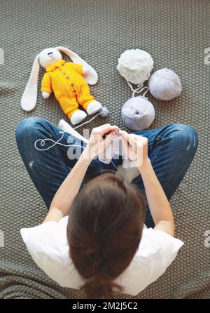 Handgefertigt und handgefertigt. Frau strickt für osterhasen, sitzt auf gestricktem grauen Karomuster. Overhead Shot femail in Freizeitkleidung Stockfoto