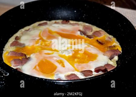 Gebratenes Eieromelett mit Speckstücken auf einer schwarzen Bratpfanne Stockfoto