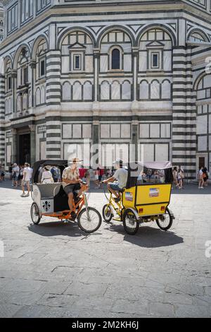 Florenz, Toskana/Italien - 15. Juni 2019: Zwei Rikscha-Fahrer, die auf ihrem Velo-Taxi vor dem Baptisterium von St. John in Florenz sitzen Stockfoto