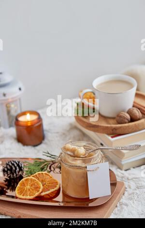 Hausgemachtes, gesalzenes Karamell in Glasgefäß mit nachgeahmtem Etikett, Weihnachtsarrangements und einer Tasse Kakao. Stockfoto