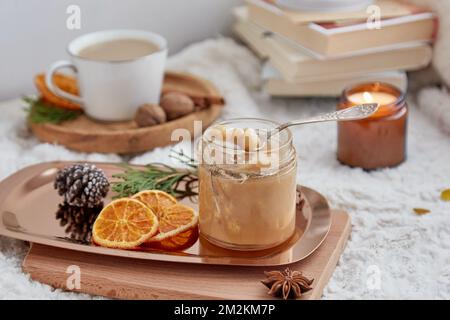 Weihnachtliches, gemütliches Frühstück. Hausgemachtes Haselnusskaramell in Glasgefäß, Kerzen, Büchern und einer Tasse Kaffee. Stockfoto