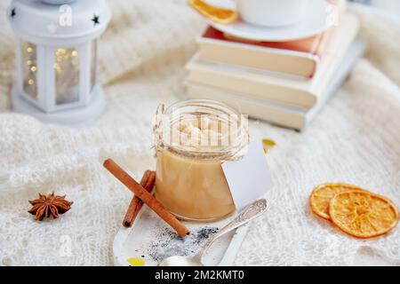 Christmas food. Homemade hazelnut salted caramel spread in glass jar with mockup label at cozy home. Stock Photo