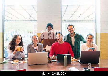 Multiethnische Gruppe junger Gelegenheitsmenschen, die Computer im Büro benutzen und vor der Kamera lächeln. Stockfoto