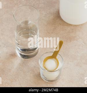 Kollagenpulver in Schale, Glas Wasser und Messlöffel auf hellbeigem Hintergrund. Zusätzliche Proteinaufnahme. Natürliche Schönheit und Gesundheit zu ergänzen Stockfoto