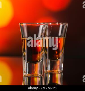 Zwei Gläser Whiskey oder Bourbon auf rotem Bokeh-Hintergrund. Whiskey-Stimmungskonzept Stockfoto