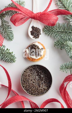 Schwarze Kaviar-Vorspeisen, Mini-Pfannkuchen auf weihnachtlich dekoriertem weißem Hintergrund, Draufsicht vertikal Stockfoto