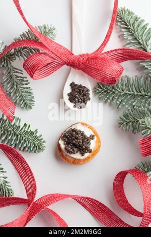 Schwarze Kaviar-Vorspeisen, Mini-Pfannkuchen auf weihnachtlich dekoriertem weißem Hintergrund, Draufsicht vertikal Stockfoto