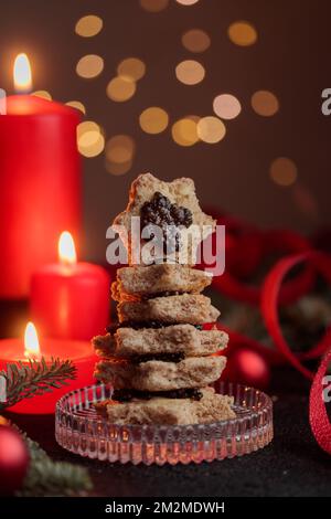 Schwarze Kaviar-Vorspeisen mit Sternen auf einem weihnachtlich dekorierten schwarzen Tisch mit roten Kerzen und Bokeh Vertical Stockfoto