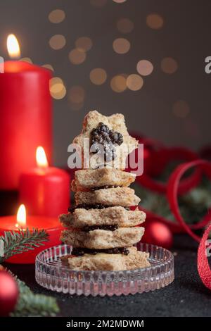 Schwarze Kaviar-Vorspeisen mit Sternen auf einem weihnachtlich dekorierten schwarzen Tisch mit roten Kerzen und Bokeh Vertical Stockfoto