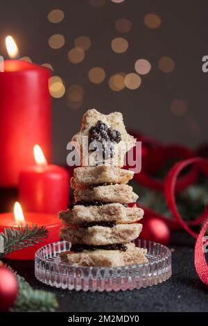 Schwarze Kaviar-Vorspeisen mit Sternen auf einem weihnachtlich dekorierten schwarzen Tisch mit roten Kerzen und Bokeh Vertical Stockfoto