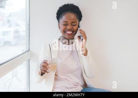 Healthy young businesswoman with glass of fresh beverage, speaking on mobile phone while consulting client sitting in cafe. Cute lady having phone Stockfoto