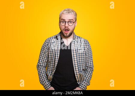 Portrait of a shocked bearded man in eyeglasses looking at camera isolated over yellow background. Stunned facial expression. Stockfoto