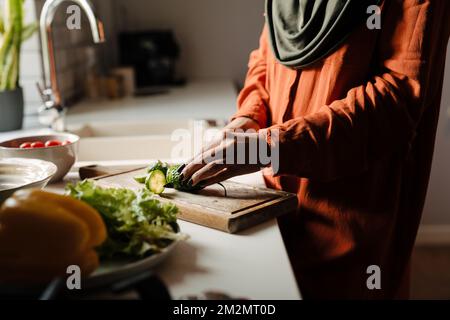 Weibliche Hände schneiden Gurke auf Holzbrett Nahaufnahme Stockfoto