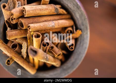 Holzschüssel, Draufsicht mit Zimtstäbchen auf dunklem Holzhintergrund. Abstrakte Lebensmittel und Kochzutaten für Dessert und gesunde Mahlzeiten Stockfoto
