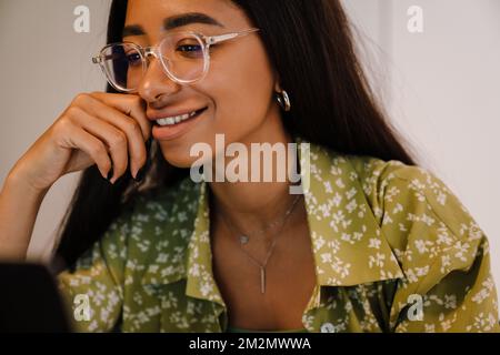 Portrait of young beautiful woman in glasses and green blouse looking on screen and touching her cheek Stockfoto
