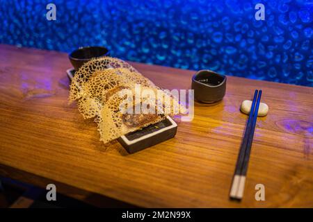 In der Pfanne gebratene Gyoza-Teigtaschen auf rustikalem Holzhintergrund im Luxusrestaurant. Exklusive Gourmetgerichte im Hintergrund. Japanische Küche im künstlerischen Design Stockfoto