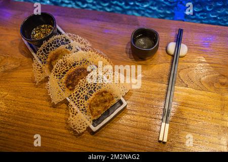 In der Pfanne gebratene Gyoza-Teigtaschen auf rustikalem Holzhintergrund im Luxusrestaurant. Exklusive Gourmetgerichte im Hintergrund. Japanische Küche im künstlerischen Design Stockfoto