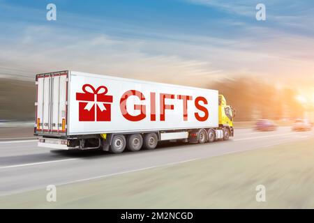 Ein Anhänger mit Container mit Symbol für die Aufschrift „Geschenke“ rast mit einer Lieferung an die Empfänger auf der Winterstraße. Das Konzept des Versendens von Geschenken für Stockfoto
