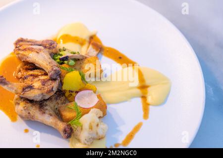 Gegrillte Hähnchenschenkel mit Gewürzen und frischem Gemüse und zerbrochenen Kartoffeln. Gourmetküche im Hintergrund mit eleganter Tischplatte und sanfter Beleuchtung Stockfoto