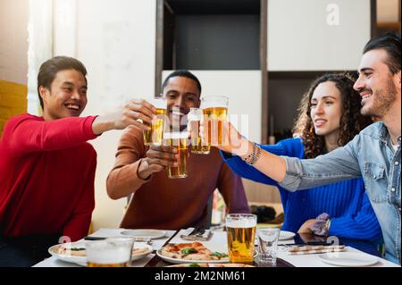 Gruppe für junge Leute, die an einem Tisch in einem Restaurant sitzen. Freunde feiern mit einem Glas Bier. Stockfoto