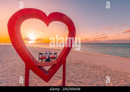 Flitterwochen-Paare-Abendessen bei einem privaten romantischen luxuriösen Abendessen am tropischen Strand auf den Malediven. Meerblick, herrliche Inselküste mit rotem Herzen Stockfoto