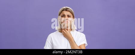 Unzufrieden junge stilvolle kaukasische Frau mit blonden Haaren und gebräunt Hautgefühl Unwohlsein im Hals mit Entzündung oder Kältegefühl Berühren Stockfoto