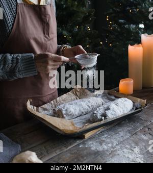 Das Mädchen streut Puderzucker auf den Weihnachtsstollen Stockfoto