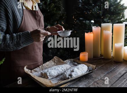 Das Mädchen streut Puderzucker auf den Weihnachtsstollen Stockfoto