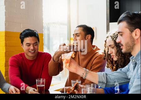 Multiethnische Gruppe von vier Personen, die Pizza am Tisch essen. Stockfoto