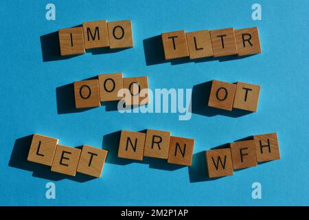 Geschäftsakronyme einschließlich IMO, TLTR, OOO, NRN, OT, LET und WFH in hölzernen Buchstaben isoliert auf blauem Hintergrund Stockfoto