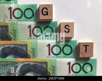 Akronym, GST Goods and Services Tax, in 3D hölzernen Buchstaben auf dem Hintergrund australischer 100-Dollar-Scheine Stockfoto