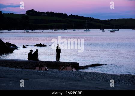 Abendlicht, das drei Personen am Strand am Polgwidden Cove am Helford River in Cornwall im Vereinigten Königreich umgibt. Stockfoto