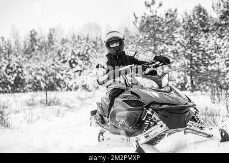 Ein Mann fährt Schneemobil in den Bergen. Fahren Sie mit einem Schneemobil in einem Bergwald. Schwarz auf Weiß Stockfoto