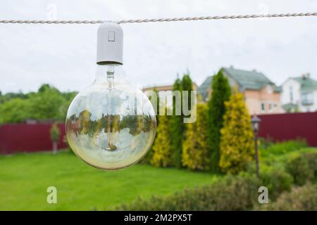 Nahaufnahme einer Glühlampe, die tagsüber auf der Straße im Garten hängt Stockfoto