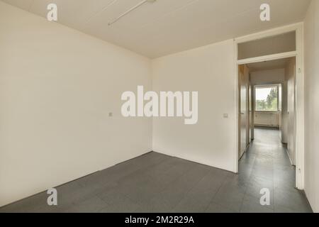 an empty room with white walls and black tiles on the floor there is a door that leads to another room Stock Photo