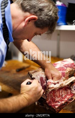 Ein Metzger bei der Arbeit, der eine Rippe Rindfleisch in einem traditionellen Metzgerladen in Salisbury UK 2022 entbeint. Stockfoto