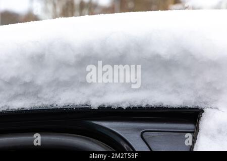 Eine dicke Schicht frischen Schnees auf dem Dach eines Pkw. Starker Schneefall erschwert Fahrern das Leben. Stockfoto