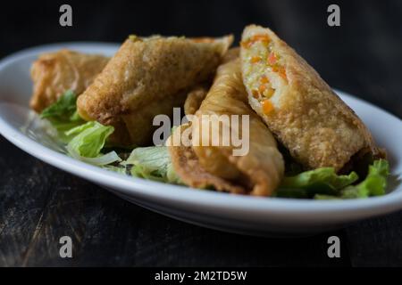 Hausgemachte Frühlingsrollen auf einem Salatbett. Auf einer weißen Platte auf einem Holzhintergrund Stockfoto