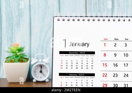 Schließen Sie den 2023. Januar Monatlicher Tischkalender für 2023 Jahr mit Wecker auf blauem Holzhintergrund. Stockfoto