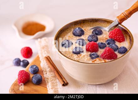 Gekochter Haferflocken aus Stahl auf Pflanzenbasis in einer Schüssel mit Heidelbeeren, Himbeeren und Zimt; Kopierbereich Stockfoto