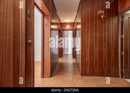 Lobby eines Hauses mit Holzwänden, Zugang zu mehreren Zimmern, goldene Wandleuchten und hellbrauner Steinzeugfußboden Stockfoto