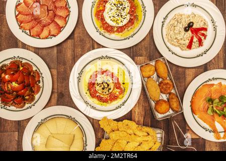 Tolles Set spanischer Gastronomiegerichte und verschiedene Tapas mit Kroketten, Tomatensalat, Kotelettwurst, russischem Salat und geräuchertem Schafskäse Stockfoto