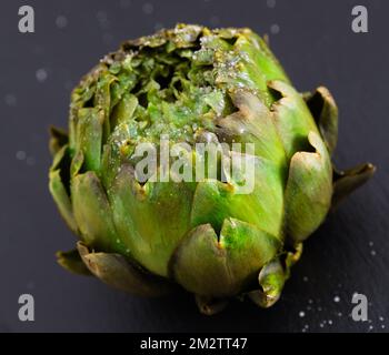 Gekochte Artischocken auf schwarzem Steinbrett Stockfoto