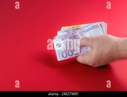 Rotes Banner mit Bargeld in der Hand eines Mannes auf rotem Tischhintergrund. Handgehaltene Euro-Banknoten. Roter Hintergrund Stockfoto