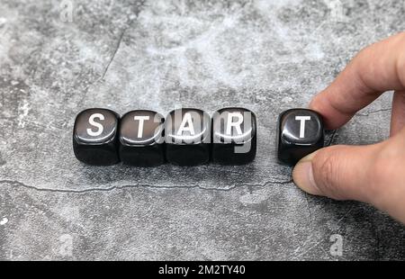 Startsymbol. Geschäftsmann dreht einen Holzwürfel und ändert das Wort 'Start' in 'Stare'. Schöner gelber Tisch, weißer Hintergrund, Kopierraum. Stockfoto