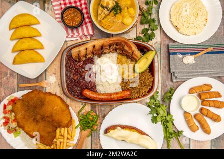 Stilleben mit typischen kolumbianischen und venezolanischen Rezepten, Bandeja paisa, Corn Empanadas, Hähnchen Clade, Arepas und tequeños und eskalieren Sie mit gebratenem Pota Stockfoto